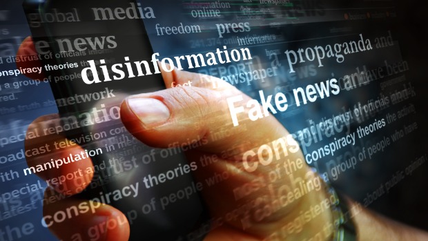 Zu sehen sind Begriffe wie Desinformation, Fake News und Verschwörungstheorien und eine Hand, die ein Handy hält.